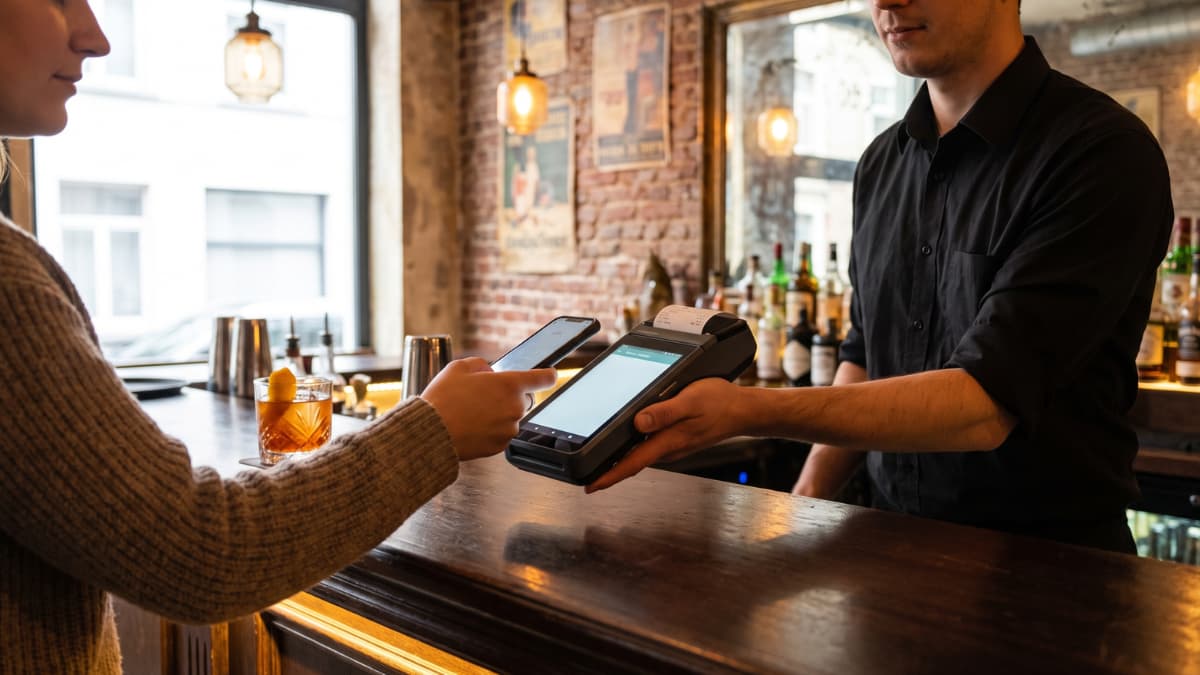 Een klant betaalt aan een bar contactloos met zijn smartphone via een draagbare betaalterminal.